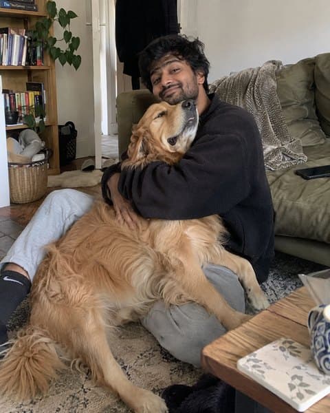 Arjun sitting on the floor of his living room hugging his golden retriever.