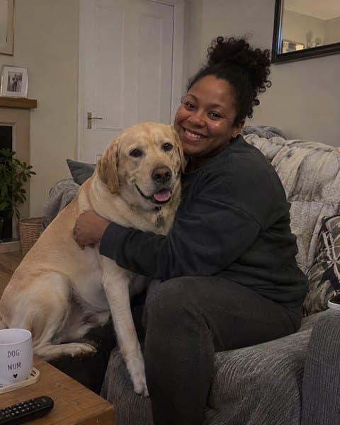 Danielle on her sofa with her arms around her labrador.