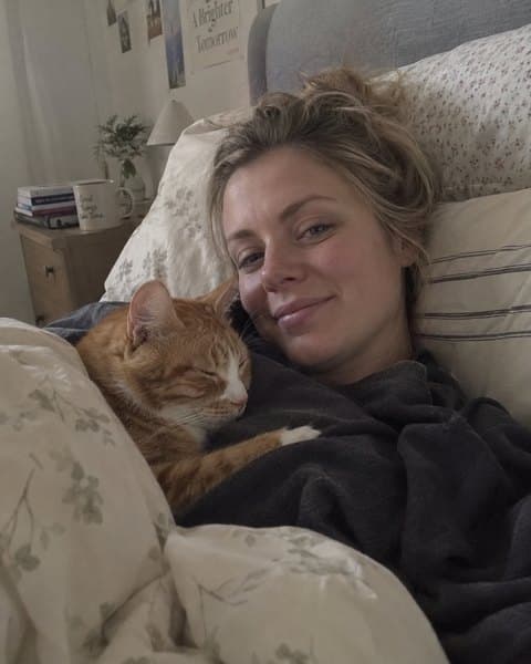 Lucy lying in bed with her ginger cat curled up beside her.