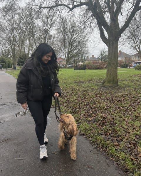 Priya walking her cockapoo through a park on a grey afternoon.
